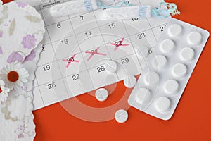 Menstrual pads and tampons on menstruation period calendar with chamomiles on red background