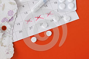 Menstrual pads and tampons on menstruation period calendar with chamomiles on red background.