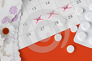 Menstrual pads and tampons on menstruation period calendar with chamomiles on red background.