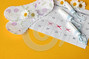 Menstrual pads and tampons on menstruation period calendar with chamomiles on yellow background