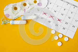 Menstrual pads and tampons on menstruation period calendar with chamomiles on yellow background