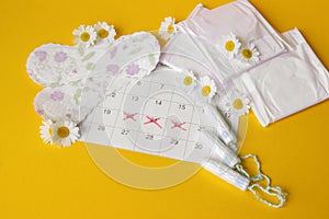 Menstrual pads and tampons on menstruation period calendar with chamomiles on yellow background.