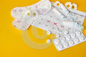 Menstrual pads and tampons on menstruation period calendar with chamomiles on yellow background.