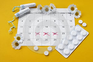 Menstrual pads and tampons on menstruation period calendar with chamomiles on yellow background.
