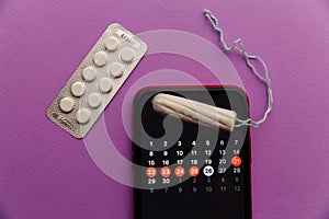 Menstruation app in smartphone with cotton tampon and red flower on a lilac background. Woman critical days and hygiene