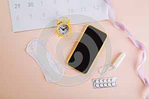 Menstruation calendar and smartphone with cotton tampon, sanitary pad and yellow alarm clock on pink background. Woman