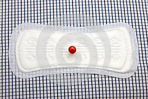 Menstruation cotton sanitary daily pad and red pin on plaid blanket. Photo for woman hygiene protection. Soft tender protection fo