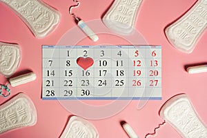 Menstruation days products, red heart and calendar with red marked dates of menstruation on pink background