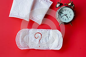 Menstruation , period delay concept with Sanitary napkin with question mark  on pad and alarm clock on red background