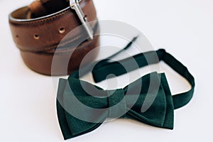 Menswear set. Men`s accessories. Green bow tie and leather belt on a white background. Wedding morning