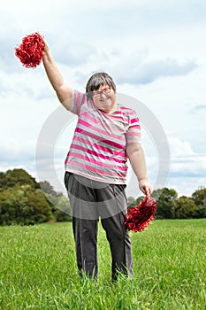 Mental disabled woman is cheering with red pompons on a green meadow