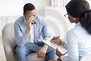 Mental health care. Professional psychotherapist having session with depressed crying young black man at clinic