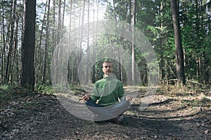 Mental health, feeling nature, mindfulness concept. Young bearded man practicing yoga outdoor, sitting in pose of lotus with eyes