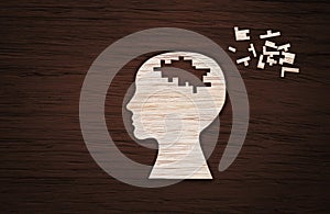 Mental health symbol. Human head silhouette with a puzzle cut out from wooden background