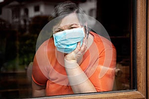 Mentally disabled woman with surgical mask looking out at window, coronavirus