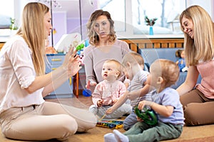 Mentor and 1 years old babies play with educational toys in kindergarten or daycare centre