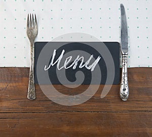 Menu written with chalk on aged blackboard with kitchen utinensil on wooden table