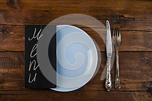 Menu written with chalk on aged blackboard with kitchen utinensil on wooden table