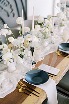 Menus lie near black plates on a festive table with white flowers on a narrow tablecloth