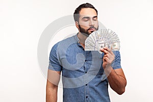 Mercantile bearded man enjoying smell of hundred dollar bills he holding, first big salary, reward for business idea