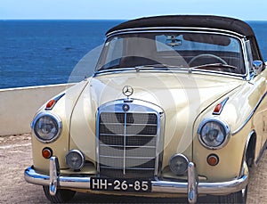 Pearlescent Mercedes Benz cabriolet convertible car in front of blue sea