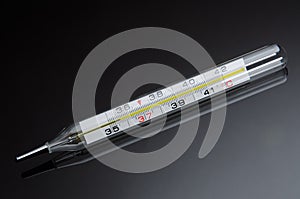 Mercury in glass thermometer on black background with reflection
