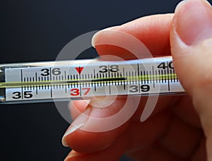 Mercury glass thermometer in a woman hand. Black background. Diagnostic of the disease