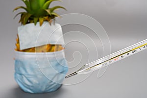 mercury thermometer about 40 degrees centigrade with a pineapple wears mask and sticks cooler pad on the forehead on background