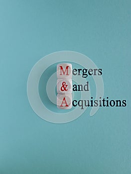 Mergers and acquisitions symbol. Concept red word mergers and acquisitions on cubes. Beautiful blue background, wooden table.
