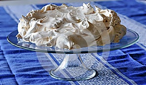 Meringue cake on a glass base placed on a table covered with a tablecloth