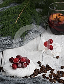 Meringue decorated with cranberries and coffee grains on a white wooden background. Glass with mulled wine and coniferous branches