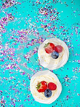 Meringue Pavlova with cream and fresh berries, strawberries, raspberries, blueberries on festive blue background with confetti,