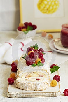 Meringue roll with butter cream and raspberry curd, decorated with berries on a light background.