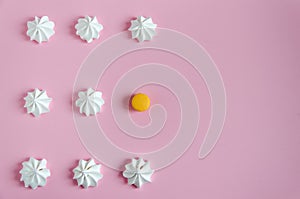 Meringue. White airy meringues laid out in rows on a pink background. The rhythmic pattern and one yellow macarone