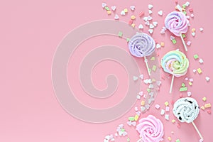 Meringues in pastel colors and scattered colorful on pink background.