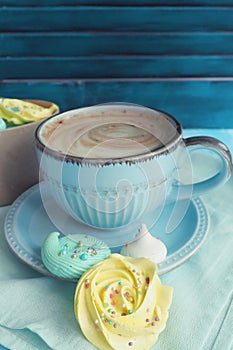 Meringues of yellow blue and white colors next to a cup of coffee on a blue cloth napkin