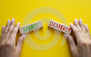 Merit or Demerit symbol. Concept word Merit or Demerit on wooden blocks. Businessman hand. Beautiful yellow background. Business
