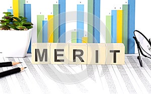 MERIT word written on wood block with chart, glasses and pencils
