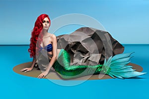 Mermaid with red hair resting near stone