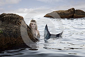 Mermaid swims in the water peeking out of the rocks