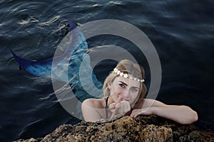 Mermaid swims in the water peeking out of the rocks