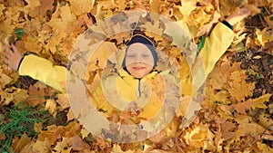 Merry autumn. The child is frolicking with maple leaves. The boy lies in yellow foliage and laughs. Happy time with
