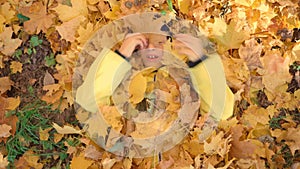 Merry autumn. The child is frolicking with maple leaves. The boy lies in yellow foliage and laughs. Happy time with