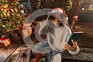 Merry Christmas. African woman in Santa hat having video chat in smartphone. Blogger in festive mood recording video in