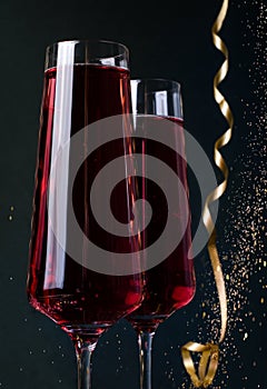 Merry Christmas background. Pink drink in glass champagne glasses with bokeh and tinsel on a black background