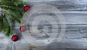 Merry Christmas background with real fir branch plus red ball ornaments on natural rustic wood