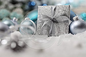 Merry christmas background, silver gift present box with bow and ribbon, next to blue Christmas balls and snowflakes, useful as a