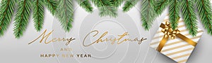 Merry Christmas banner or header. White present box with golden bow under green fir tree branches on silver background