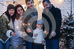 Merry Christmas. Big happy family standing in snow-covered house yard with lit sparklers in hands