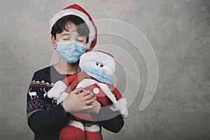 Merry Christmas, boy with medical mask hugging his snowman toy